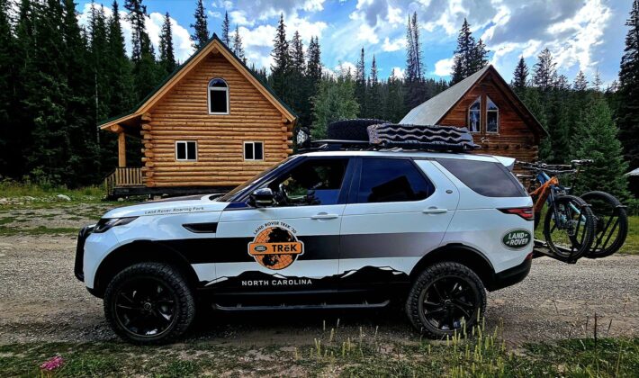 photo of a white Land Rover Discovery 5 in front of some cabins