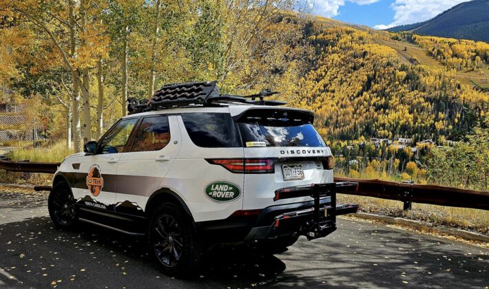 photo of a white Land Rover Discovery 5 in front of a scenic fall landscape